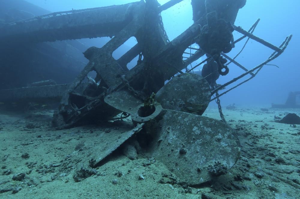 Underwater photograph of a large ship propeller and hull structure lying on the seabed.